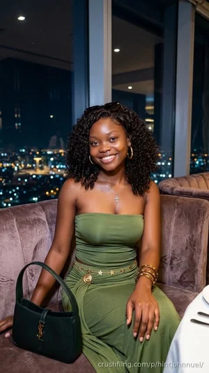 Woman in green strapless dress sitting on velvet couch with city lights behind her.