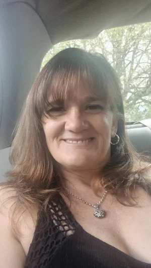 Woman with shoulder-length brown hair in a black lace top, smiling in a car.