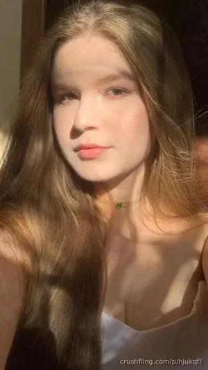 Woman with long brown hair wearing a white top, indoors in soft lighting.