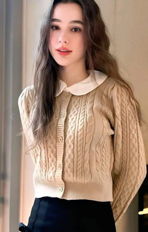 Woman with long brown hair wearing beige cardigan with white collar indoors.
