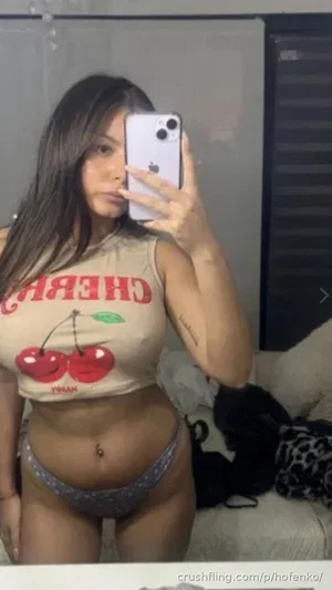 Woman in cherry-print crop top and patterned underwear taking mirror selfie in bedroom.