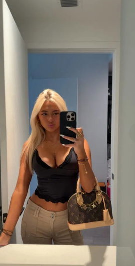 Blonde woman in black top taking mirror selfie indoors.