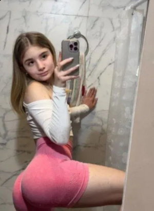 Curvy woman in pink shorts and white top taking bathroom selfie.