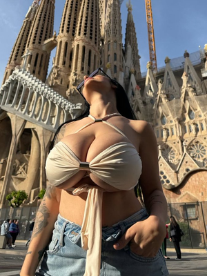 Woman in beige top and jeans poses outdoors in front of ornate cathedral.