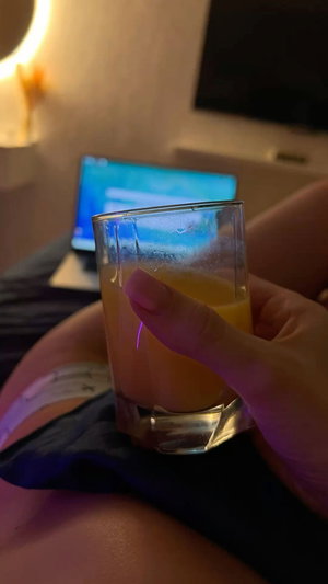 Woman holding orange drink on bed in bedroom.