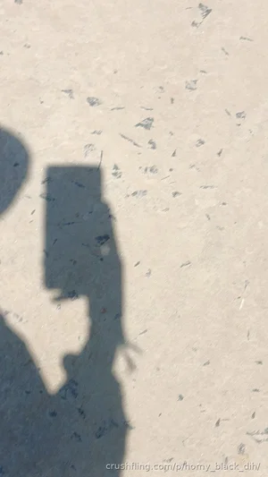 Shadow of a person holding a phone on a textured ground surface.