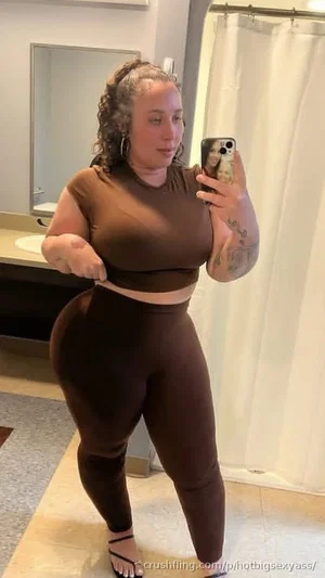 Woman in brown crop top and leggings takes mirror selfie in bathroom.