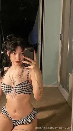 Woman in black and white checkered lingerie taking mirror selfie in bedroom.
