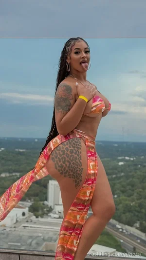 Woman in colorful bikini and wrap, posing on balcony with city view.