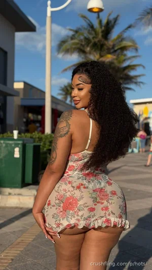 Woman with curly hair and back tattoo wearing floral mini dress outdoors.
