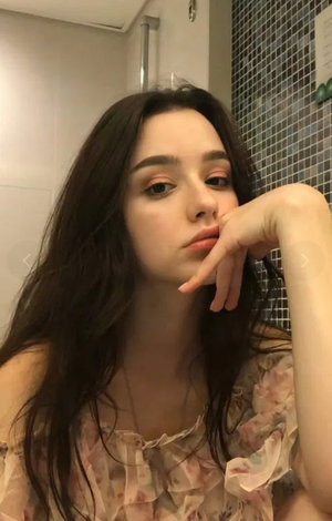 Woman with long dark hair in floral top in bathroom.