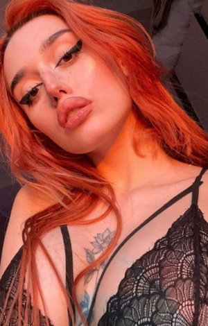 Red-haired woman in black lace lingerie taking indoor selfie.