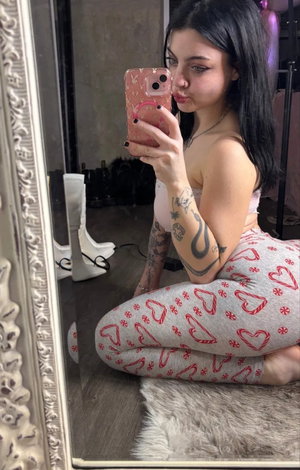 Dark-haired woman with tattoos taking mirror selfie indoors.