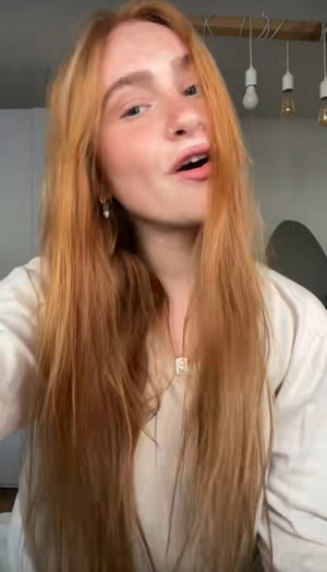 Woman with long red hair wearing white top indoors.