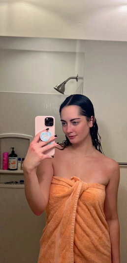 Woman with wet dark hair wrapped in orange towel in bathroom.