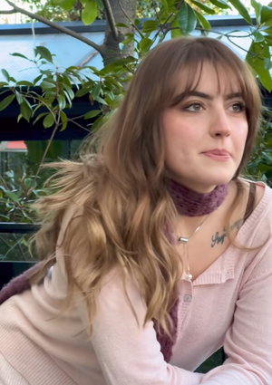 Woman with long brown hair wearing pink sweater outdoors.