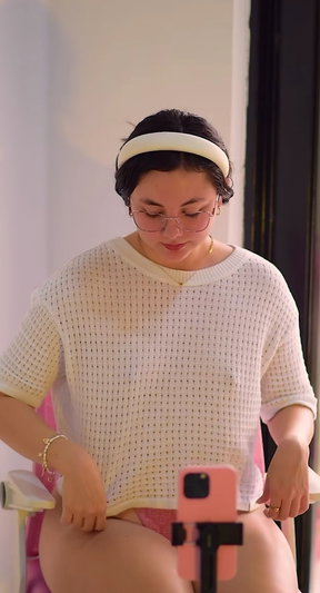 Woman with glasses and headband in mesh top taking selfie indoors.
