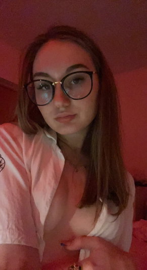 Woman with glasses and brown hair in a white shirt, indoors, holding shirt open slightly.