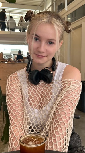 Blonde woman with space buns wearing mesh top in cafe.