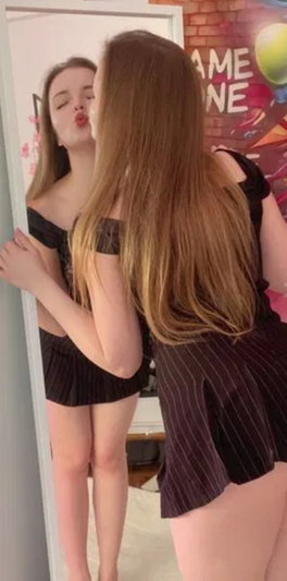 Long-haired woman in black top and striped skirt mirror selfie.