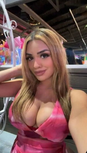 Woman with long blonde hair in pink dress taking indoor selfie.