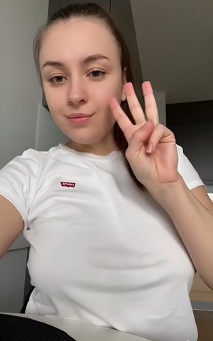 Woman with ponytail in white t-shirt, peace sign, indoor.