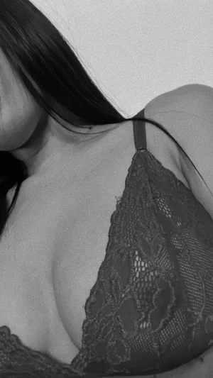 Woman with dark hair wearing black lace bra, close-up of chest and shoulder.