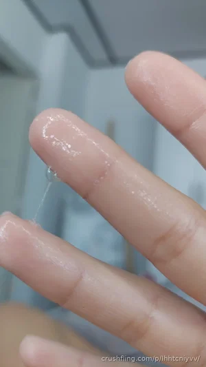 Close-up of fingers with clear liquid droplet, blurred background.