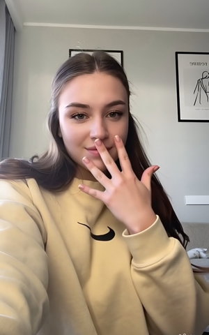 Woman with long brown hair in beige Nike sweatshirt indoors.