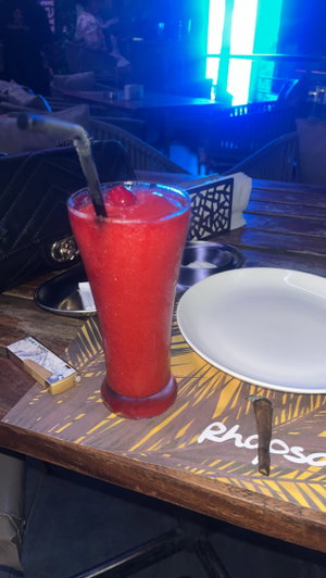 Red frozen cocktail on wooden table in dimly lit bar.