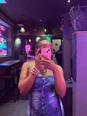 Woman in denim taking mirror selfie in neon bar.