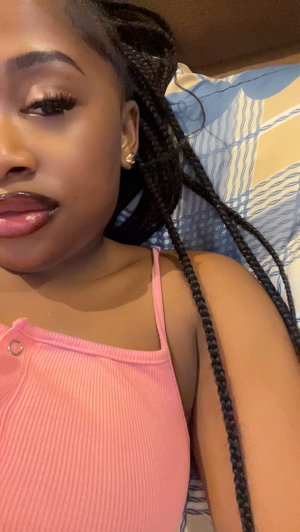 Woman with braids in pink top lying on bed.