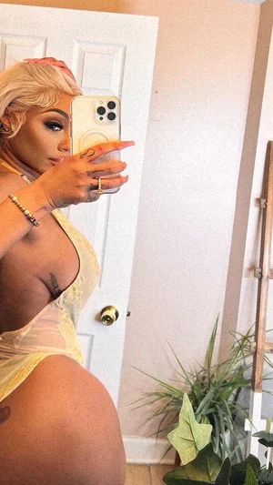 Woman with blonde hair in yellow lace lingerie taking mirror selfie indoors.