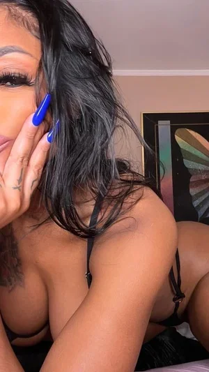 Woman with dark hair and blue nails in black lingerie, posing indoors.