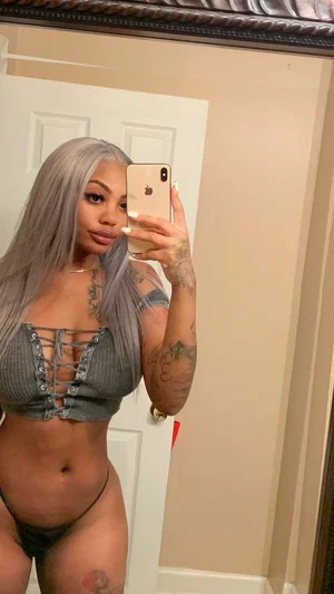 Woman with gray hair and tattoos wears gray lace-up top and black underwear, taking mirror selfie
