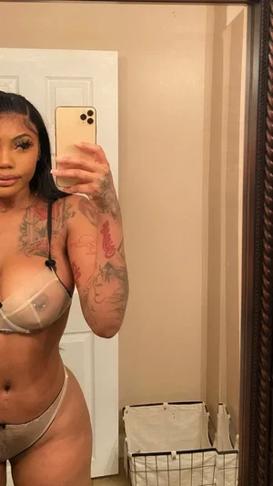 Woman with tattoos in sheer lingerie taking mirror selfie indoors.