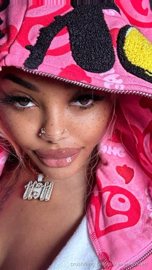 Woman with pink hair and freckles wearing a pink patterned hoodie, close-up selfie.