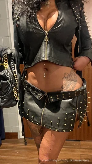 Woman in black studded leather outfit with tattoos, standing indoors.