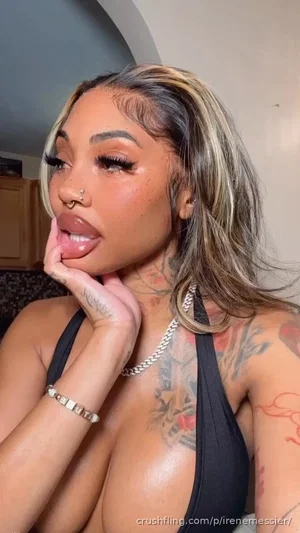 Woman with tattoos, black top, and silver jewelry posing indoors.