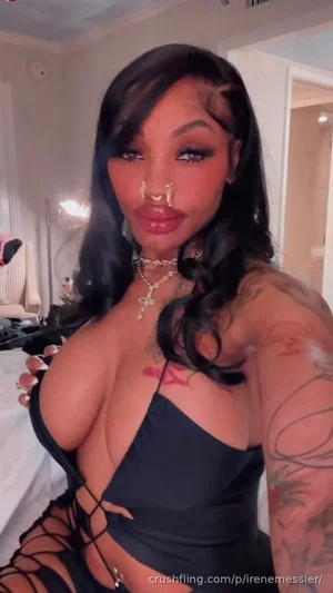 Woman with long black hair and tattoos wearing black lace-up top in bedroom.
