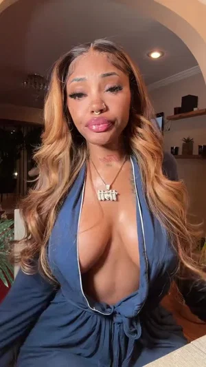 Woman with long wavy hair in a blue plunging top, indoors, facing camera.