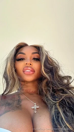 Woman with long wavy hair, tattoos on shoulder, wearing cross necklace, bare shoulders.
