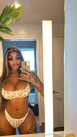 Woman in floral bikini taking mirror selfie indoors, tattoos visible, long hair.