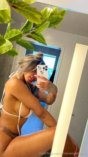 Woman with tattoos in white lingerie taking mirror selfie indoors.