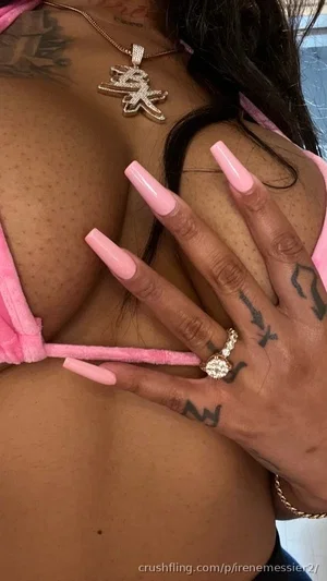 Woman with tattoos and long pink nails wearing pink lingerie, hand near chest.