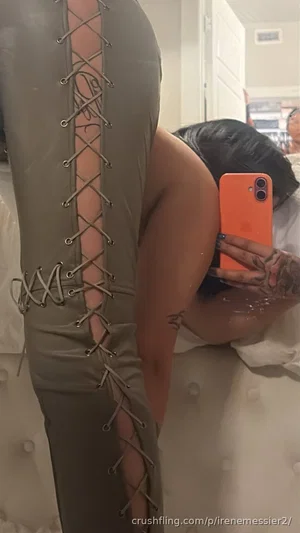 Woman in olive green lace-up bodysuit taking mirror selfie in bedroom.