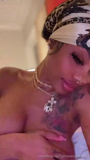 Woman with tattoos and jewelry, wearing a headscarf, posing indoors.