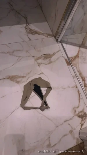 A beige and black bra lies on a marble bathroom floor.