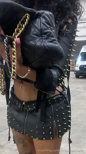 Woman in black studded leather outfit with tattoos, standing outdoors.