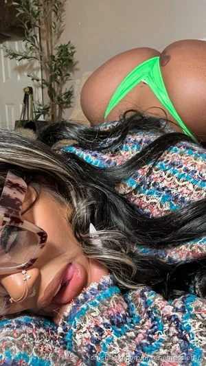 Woman with long dark hair and glasses lying on a colorful blanket, wearing a bright green thong.